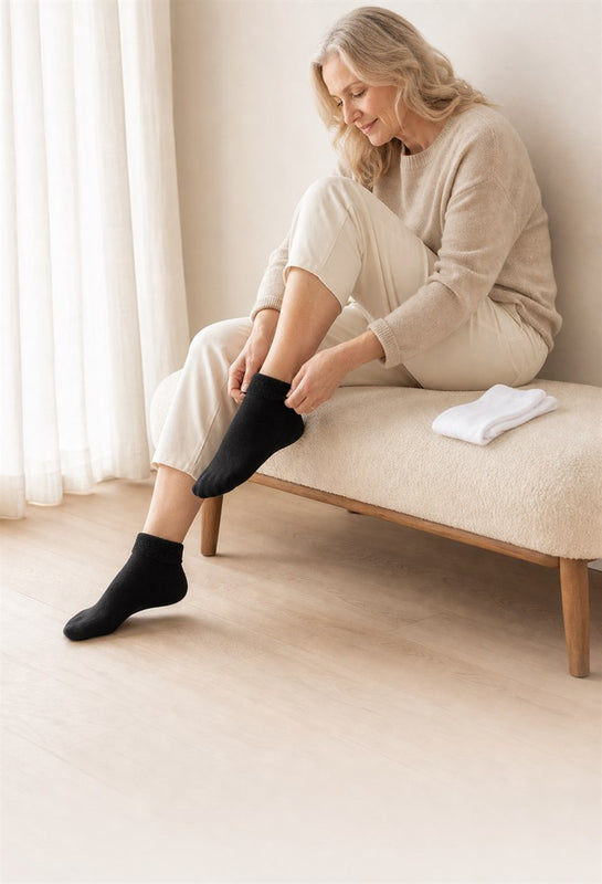 Woman putting on soft black comfort socks in a calm modern bedroom